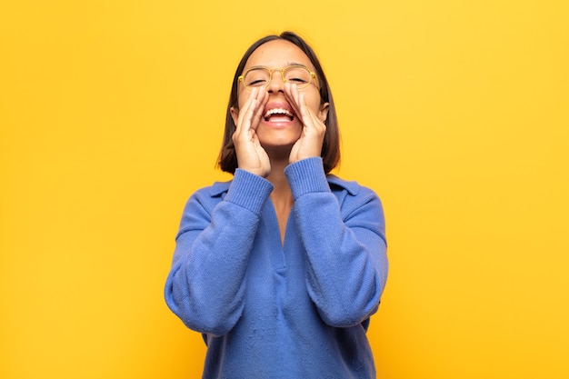 Mujer latina joven que se siente feliz, emocionada y positiva, dando un gran grito con las manos al lado de la boca, gritando