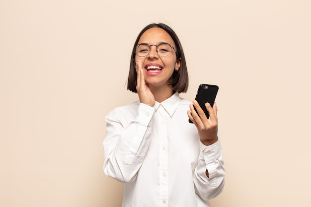 Mujer latina joven que se siente feliz, emocionada y positiva, dando un gran grito con las manos al lado de la boca, gritando