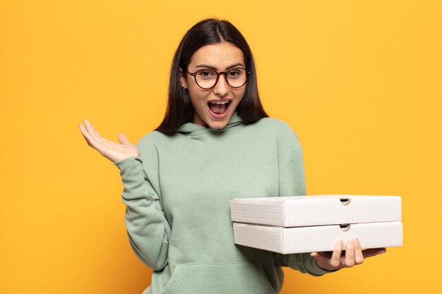 Mujer latina joven que se siente feliz, emocionada, sorprendida o conmocionada, sonriendo y asombrada por algo increíble