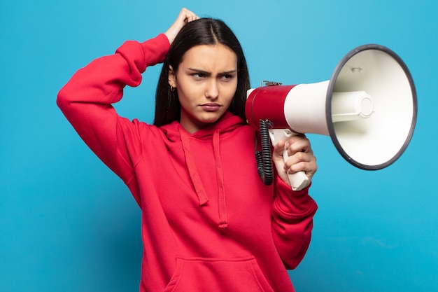 Foto mujer latina joven que se siente perpleja y confundida, rascándose la cabeza y mirando hacia un lado