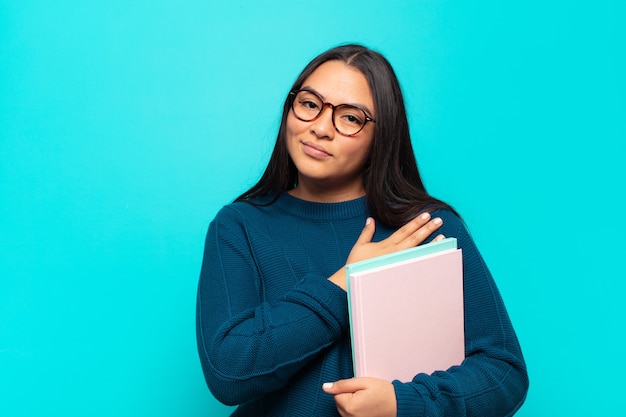 Mujer latina joven que se siente romántica, feliz y enamorada, sonriendo alegremente y tomados de la mano cerca del corazón