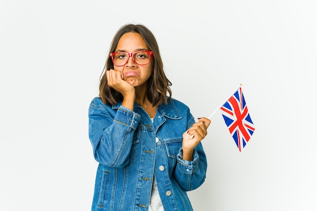 Mujer latina joven que sostiene una bandera inglesa aislada en la pared blanca que se siente triste y pensativa, mirando el espacio de la copia.