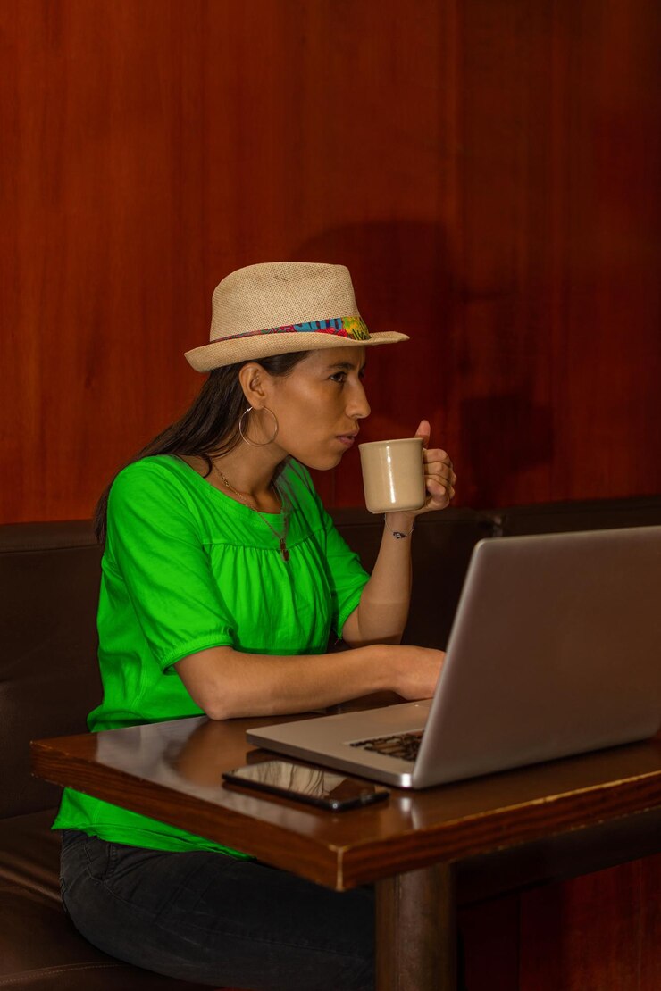 Foto mujer latina joven que trabaja en su computadora portátil mientras bebe una taza de café
