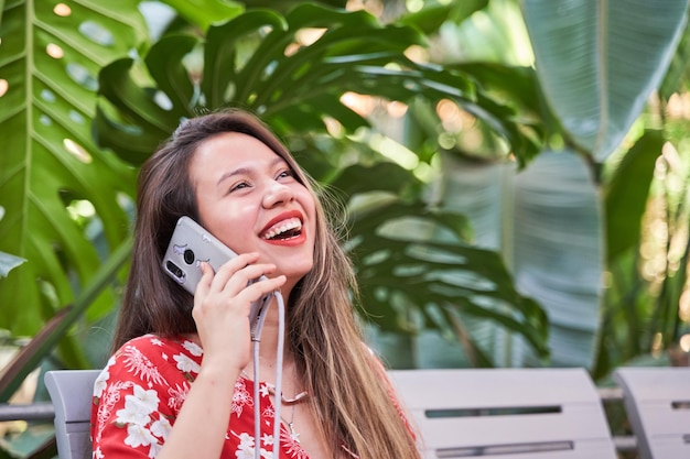 Mujer latina joven riendo mientras habla por su teléfono celular en un parque