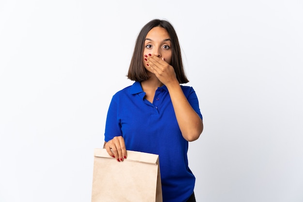 Mujer latina joven sosteniendo una bolsa de compras aislada en blanco coning boca con las manos