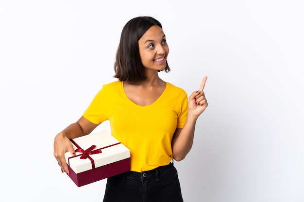 Mujer latina joven sosteniendo un regalo aislado apuntando hacia una gran idea