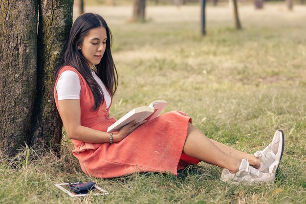 Mujer latina leyendo un libro ornamentado de un árbol en el parque