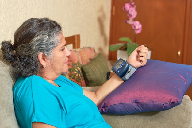 Mujer latina madura comprueba su presión arterial desde casa Concepto de hipertensión