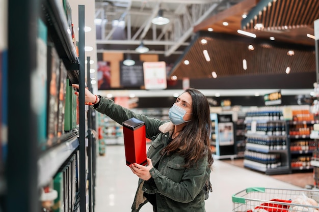 Mujer latina madura con mascarilla eligiendo o comprando bebida en un supermercado