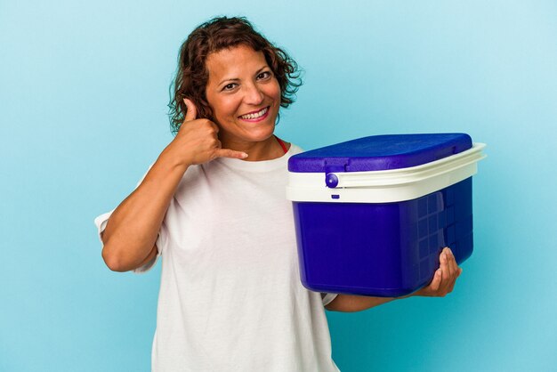 Mujer latina de mediana edad aislada sobre fondo azul que muestra un gesto de llamada de teléfono móvil con los dedos.