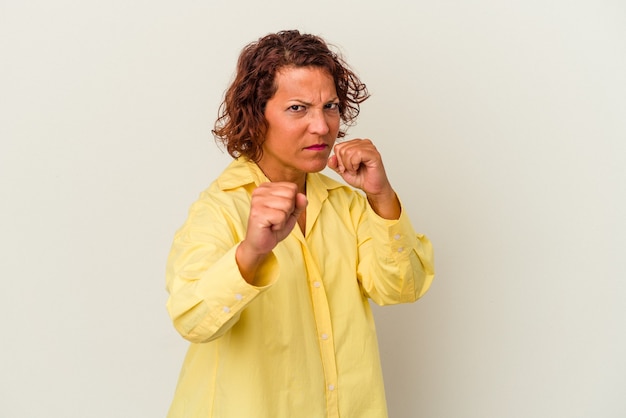 Mujer latina de mediana edad aislada sobre fondo blanco lanzando un puñetazo, ira, luchando debido a una discusión, boxeo.