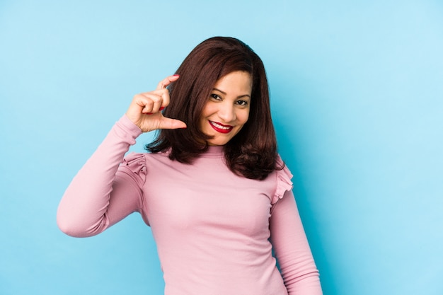 Mujer latina de mediana edad aislada sosteniendo algo poco con los dedos índices, sonriente y confiado.