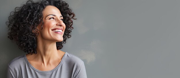 Mujer latina de mediana edad con una expresión positiva parada sola y contemplando un fondo gris