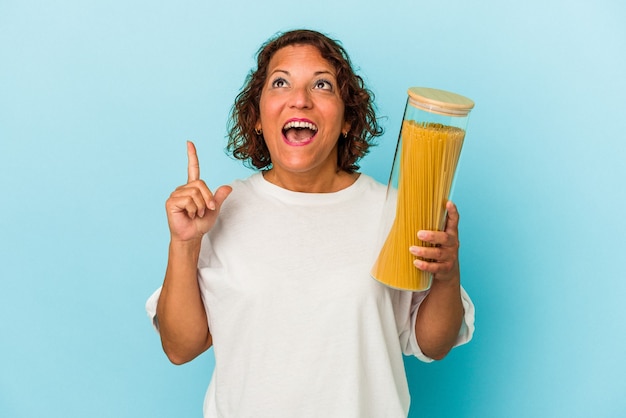 Mujer latina de mediana edad sosteniendo frasco de pasta aislado sobre fondo azul apuntando al revés con la boca abierta.