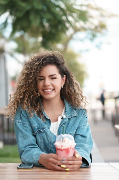 Mujer latina mirando a la cámara mientras bebe una bebida fría en un café al aire libre