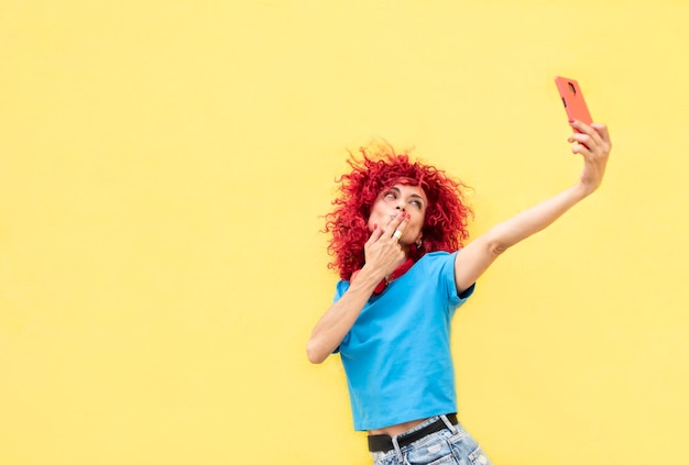 Foto mujer latina con pelo afro rojo en un fondo amarillo se toma un selfie con su teléfono móvil