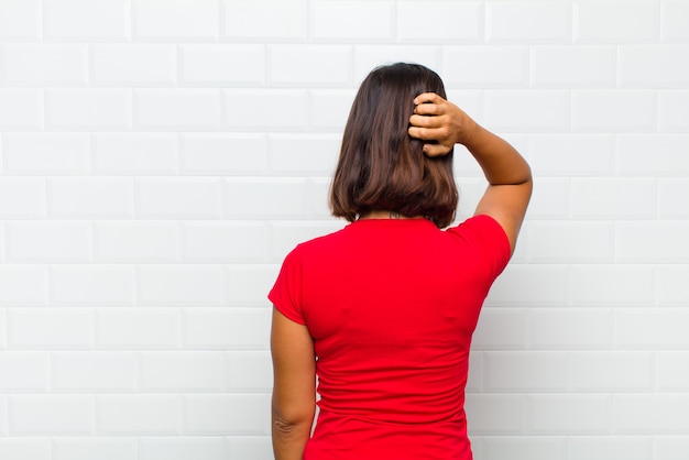 Foto mujer latina pensando o dudando, rascándose la cabeza, sintiéndose desconcertado y confundido, vista trasera o trasera