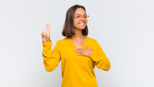 Mujer latina que parece feliz, segura y digna de confianza, sonriendo y mostrando el signo de la victoria, con una actitud positiva