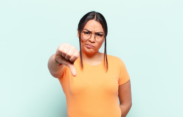 Mujer latina que se siente enfadada, enojada, molesta, decepcionada o disgustada, mostrando los pulgares hacia abajo con una mirada seria.