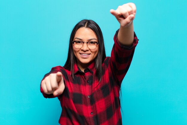 Foto mujer latina que se siente feliz y segura, apuntando a la cámara con ambas manos y riendo, eligiéndote