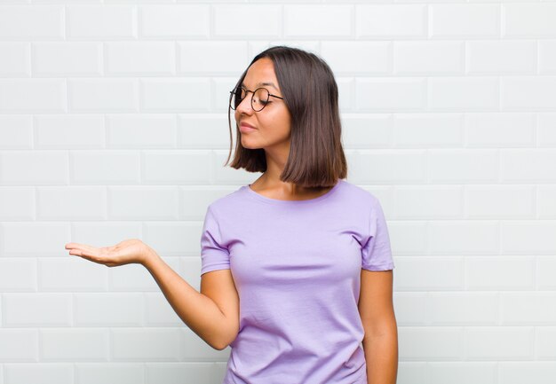 Mujer latina que se siente feliz y sonriendo casualmente, mirando un objeto o concepto sostenido en la mano al costado