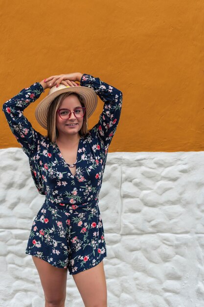 Mujer latina con sombrero y gafas al aire libre sobre un fondo amarillo y blanco