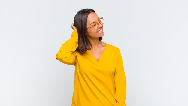 Mujer latina sonriendo alegre y casualmente, tomando la cabeza con una mirada positiva, feliz y segura