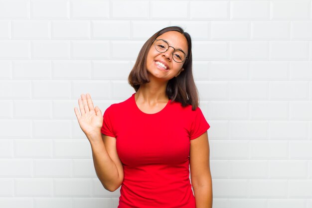 Foto mujer latina sonriendo feliz y alegremente, saludando con la mano, dándote la bienvenida y saludándote, o diciéndote adiós