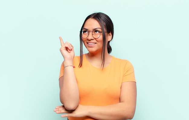 Mujer latina sonriendo felizmente y mirando hacia los lados, preguntándose, pensando o teniendo una idea