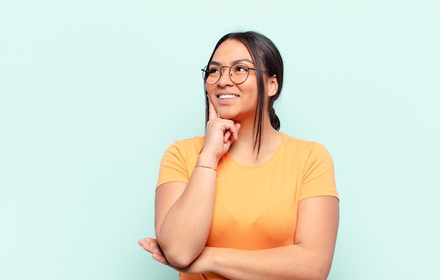 Mujer latina sonriendo felizmente y soñando despierto o dudando, mirando hacia el lado