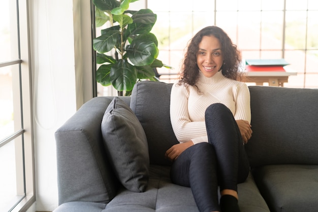 Mujer latina sonriendo y sentado en el sofá en casa