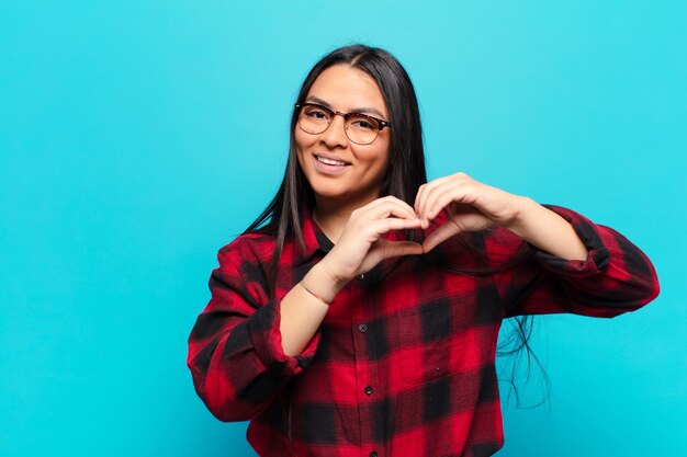 Mujer latina sonriendo y sintiéndose feliz, linda, romántica y enamorada, haciendo forma de corazón con ambas manos