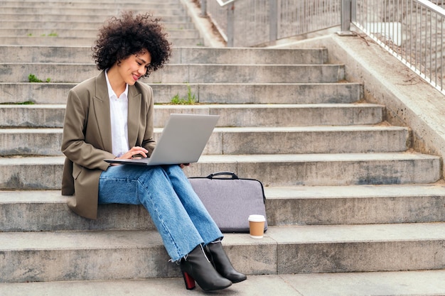 Mujer latina sonriente que trabaja con la computadora al aire libre