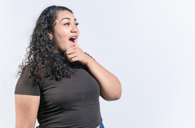 Mujer latina sorprendida sosteniendo la barbilla mirando un anuncio al lado Mujer latina asombrada con la mano en la barbilla mirando al lado aislado