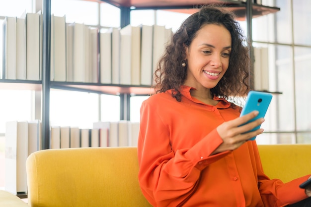 Mujer latina con teléfono móvil o smartphone y sosteniendo tablet oat home