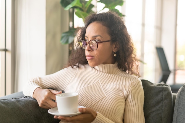 Mujer latina tomando café en el sofá en casa