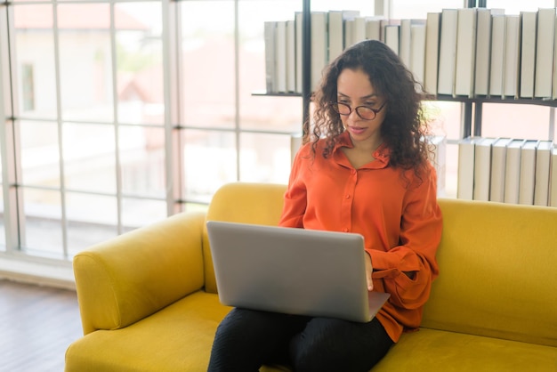 mujer latina, trabajando, con, computador portatil, sofá, en casa