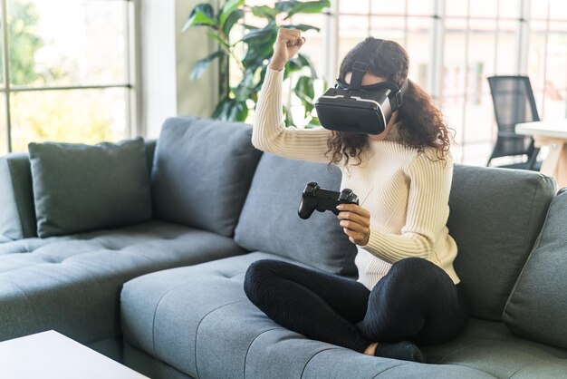 Mujer latina usando un casco de realidad virtual en el sofá en casa