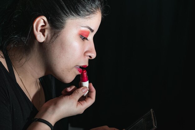 Mujer latina usando un pintalabios para pintarse los labios de rojo abriendo un poco la boca para aplicar el pintalabios