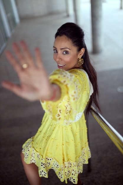 Mujer latina con vestido amarillo se cubre con la mano.