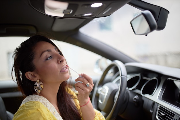 Mujer latina en vestido amarillo pintando sus labios dentro de un coche.