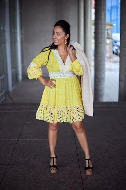 Mujer latina en vestido amarillo posando en una calle de la ciudad.