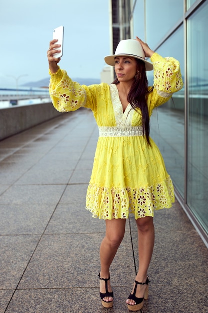 Mujer latina en vestido amarillo tomando un selfie en la calle.