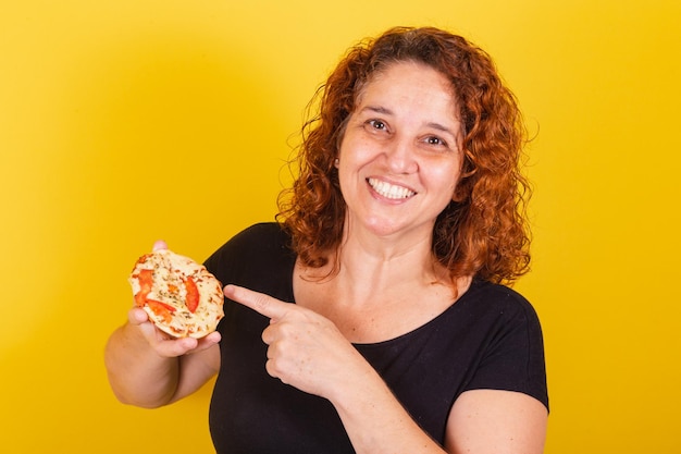 Mujer latinoamericana brasileña caucásica cabello rizado rizos fondo amarillo que muestra la presentación ofreciendo mini pizza comer pizza comer margarita pizza queso estiramiento delicioso