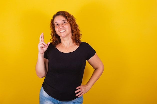 Mujer latinoamericana brasileña caucásica cabello rizado rizos fondo amarillo signo de suerte suerte dibujar los dedos cruzados lotería deseando vítores