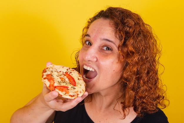 Mujer latinoamericana brasileña caucásica rizos de pelo rizado fondo amarillo comer mini pizza comer pizza comer margarita pizza queso estiramiento delicioso