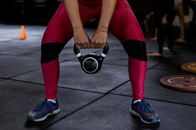 Mujer latinoamericana de pie con las piernas abiertas sosteniendo pesas rusas con ambas manos durante su entrenamiento en el gimnasio Concepto de estilo de vida saludable irreconocible