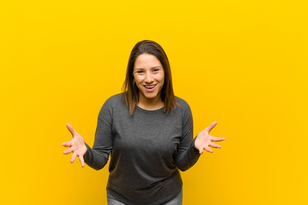 Mujer latinoamericana que se siente feliz, asombrada, afortunada y sorprendida, ¿como decir omg en serio? Increíble aislado en pared amarilla