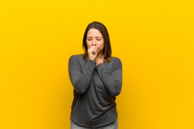 Mujer latinoamericana sintiéndose enferma con dolor de garganta y síntomas de gripe, tos con la boca cubierta aislada