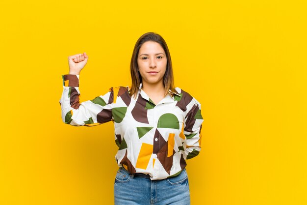 Mujer latinoamericana sintiéndose seria, fuerte y rebelde, levantando el puño, protestando o luchando por la revolución aislada contra la pared amarilla